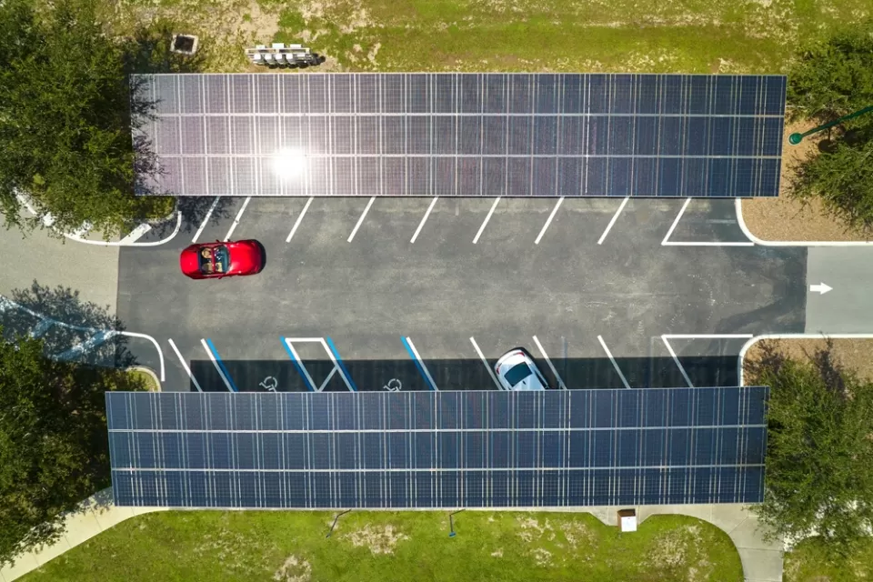 Overhead view of parking lot with solar panel canopies over parking spots and red car driving in